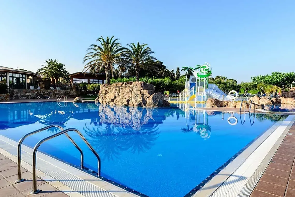 Piscine bleue vive à ESTIVAL: Corporative avec toboggan et palmiers.