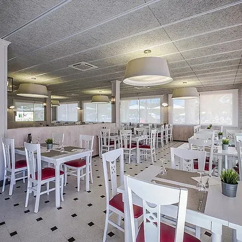 Restaurante luminoso con mesas blancas y sillas rojas en Estival Vendrell Platja, Baix Penedès.