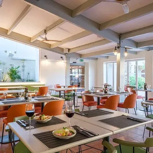 ESTIVAL: Corporate dining area with set tables, orange chairs, and garden view.