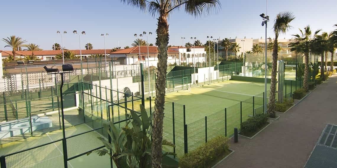 una cancha de tenis está rodeada de palmeras y edificios