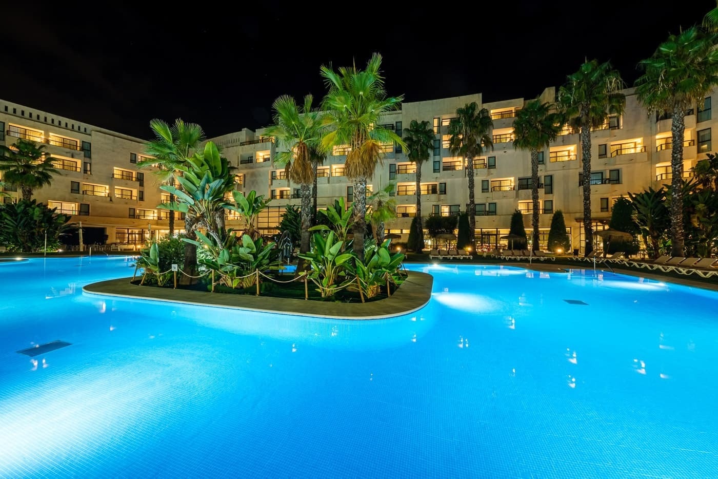 a large swimming pool in front of a hotel at night