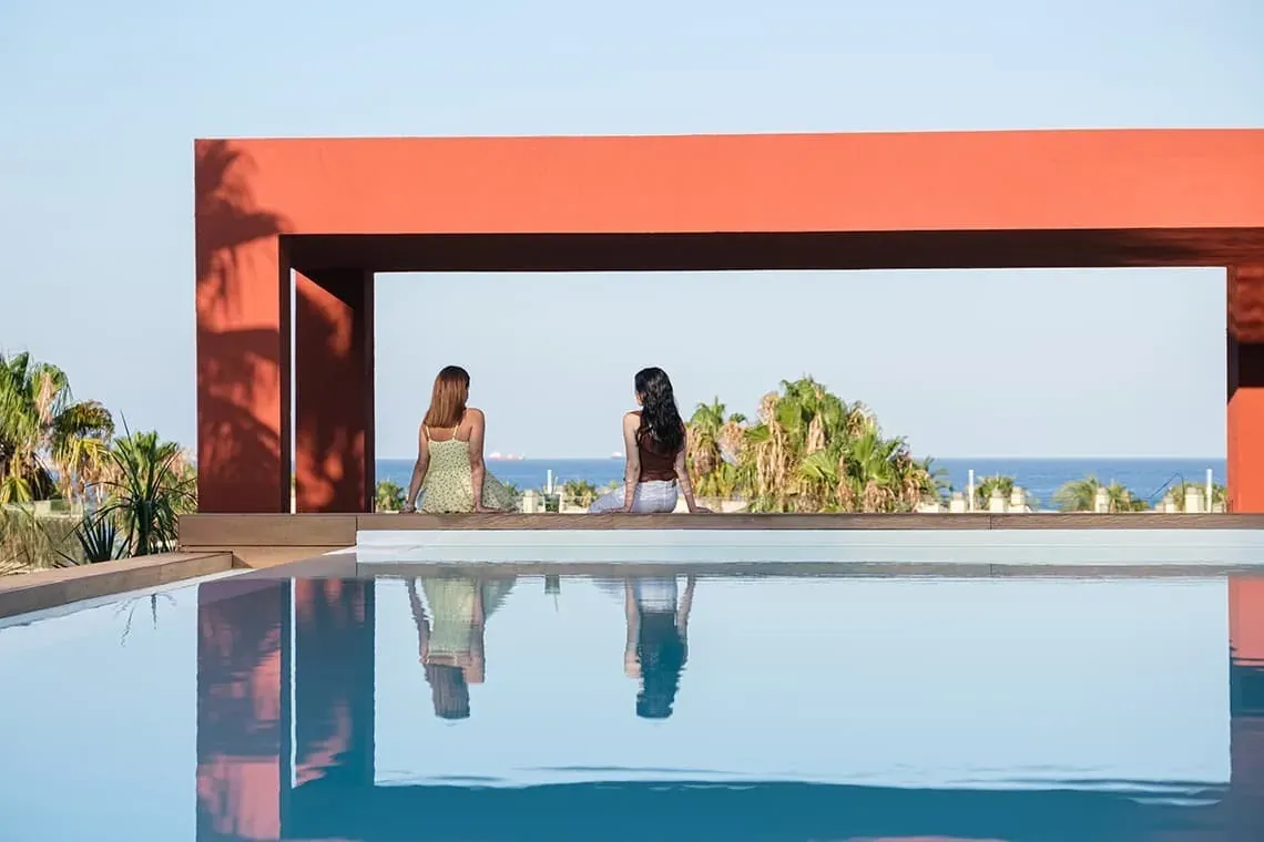 dos mujeres se sientan en el borde de una piscina mirando al océano