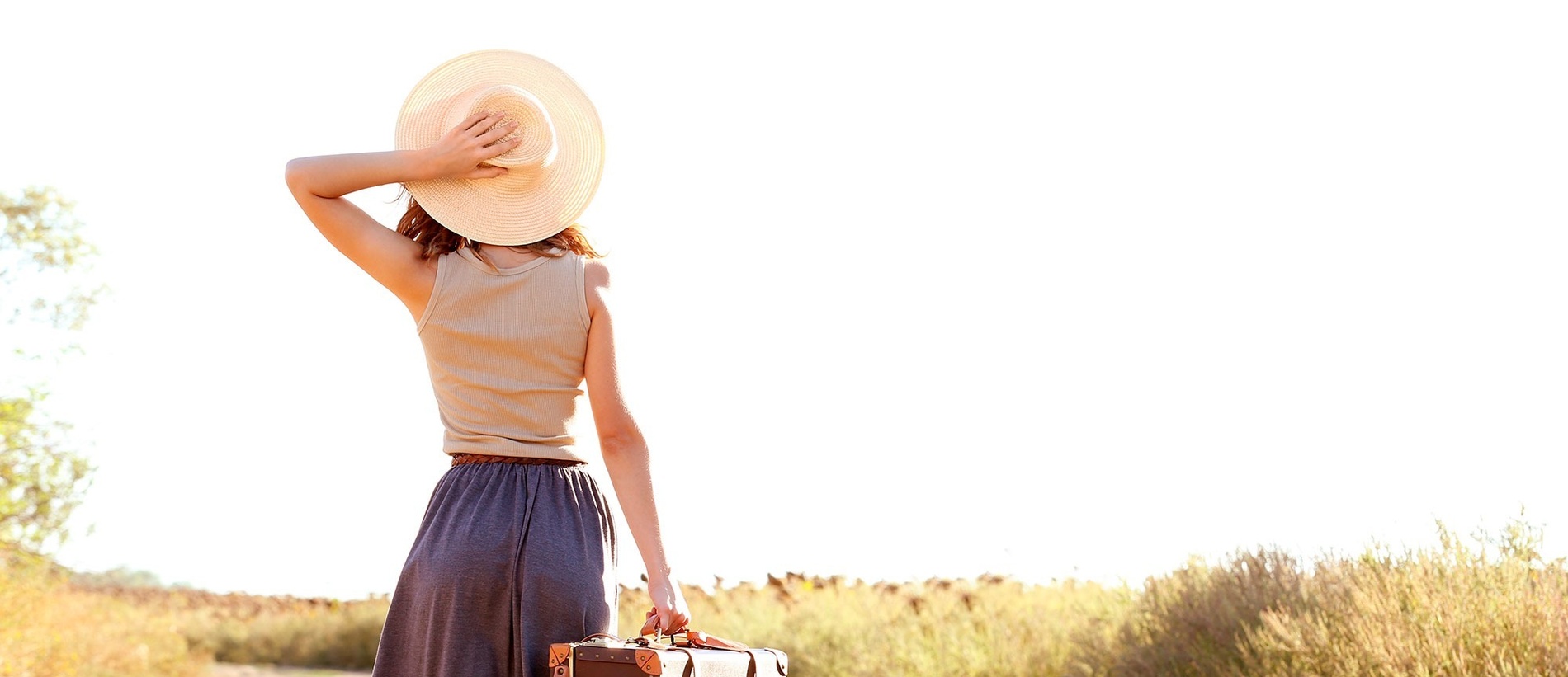 a woman wearing a hat holds a suitcase in a field