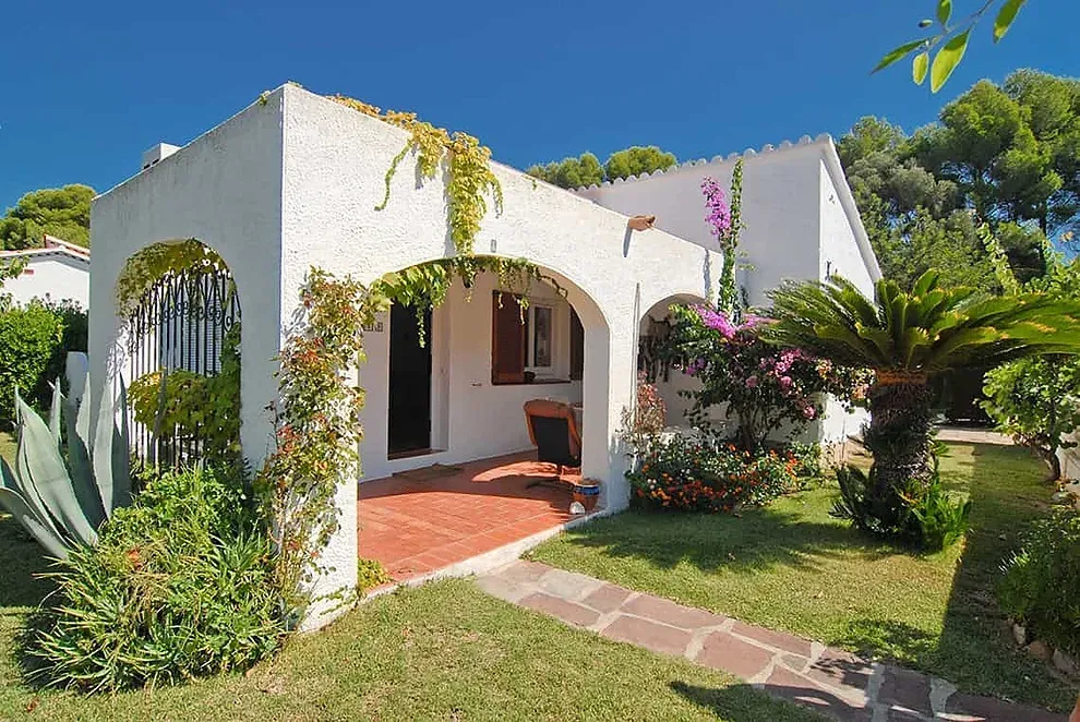 Villa ESTIVAL: Corporativa con porche, jardín y palmera bajo cielo azul.