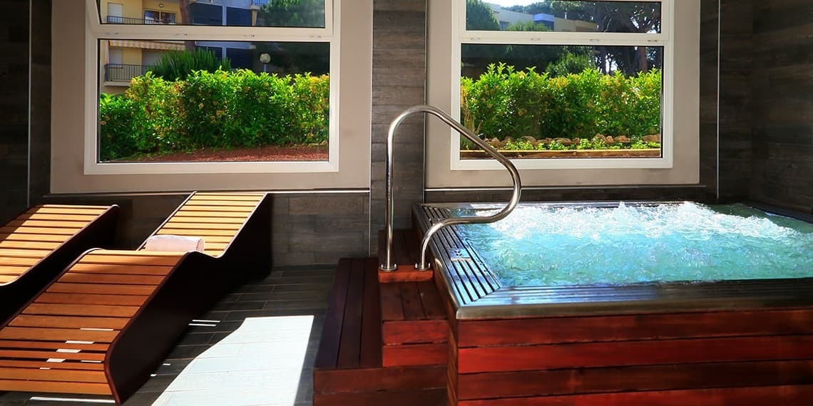 una bañera de hidromasaje está rodeada de sillas de madera y dos ventanas