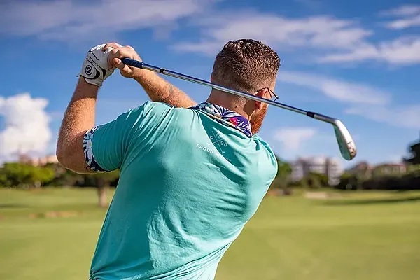 Golfer swinging a club on a green course, ideal for ESTIVAL: Corporate.