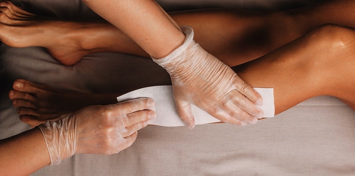 una mujer se está depilando las piernas con guantes de plástico