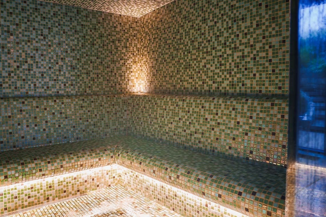 una mujer envuelta en una toalla está sentada en una ducha de vapor .