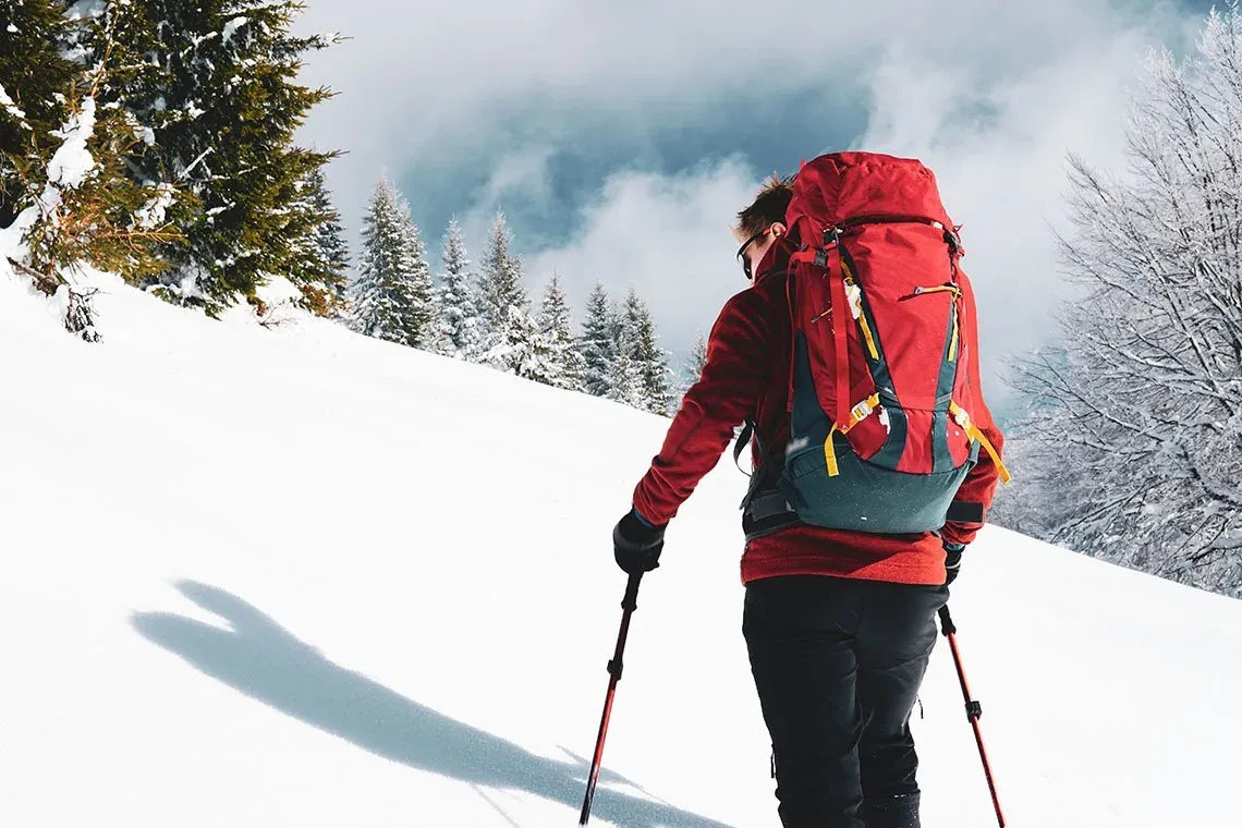 um homem com uma mochila vermelha caminha pela neve