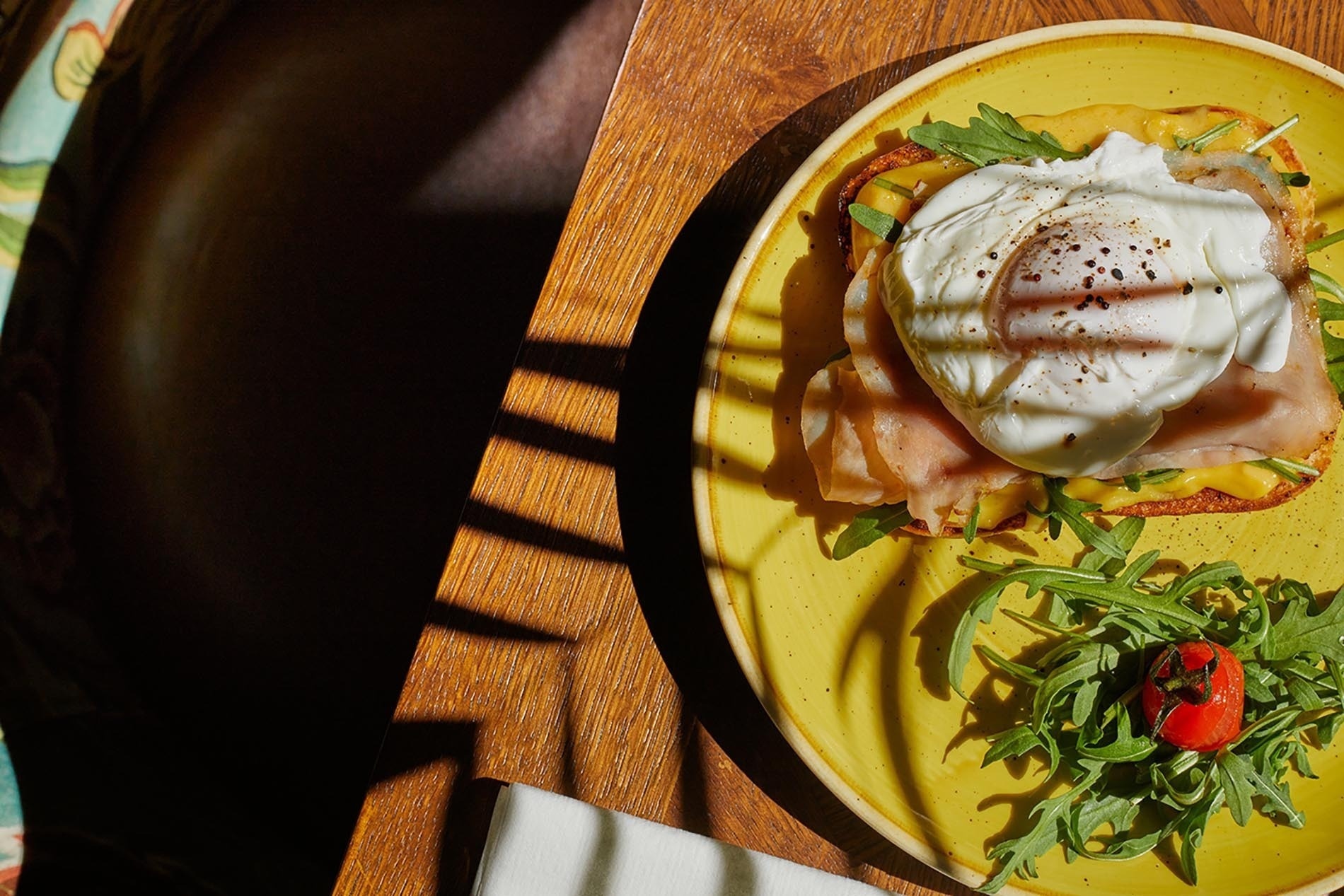 un plato amarillo con un huevo escalfado y jamón encima