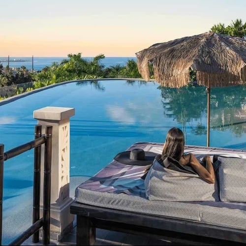 a woman sits on a couch near an infinity pool