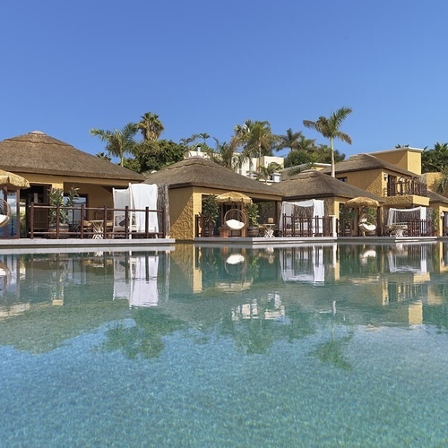 Eine Gruppe von Hütten mit Strohdach steht neben einem großen Swimmingpool