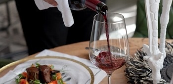 eine Person gießt Wein in ein Glas neben einem Teller mit Essen