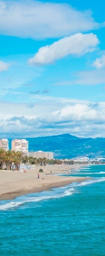 una playa llena de gente en un día soleado con montañas en el fondo .