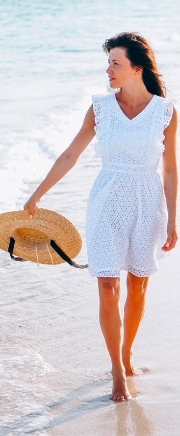 a woman in a white dress is walking on the beach holding a straw hat