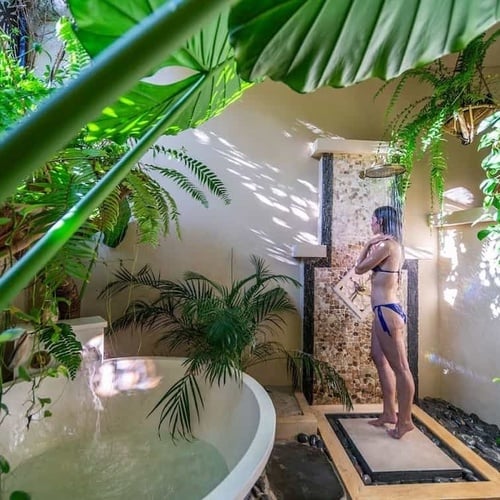 a woman in a bikini is taking a shower in a bathroom surrounded by plants