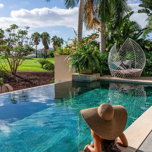 a woman in a hat sits on the edge of an infinity pool