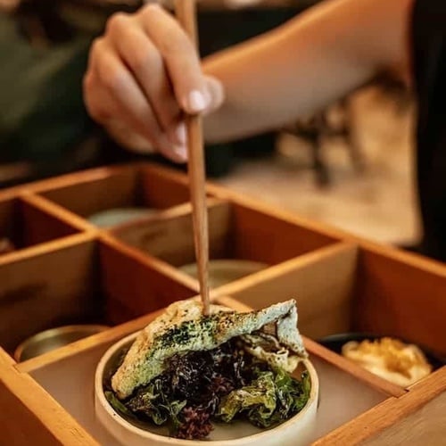 a person is eating a sandwich with chopsticks in a wooden box .