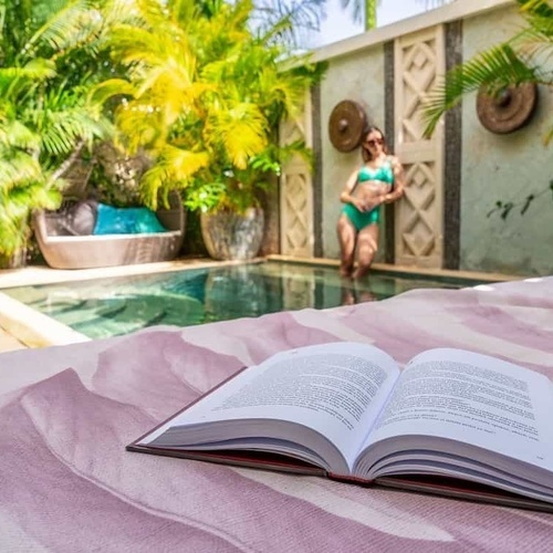 eine Frau in einem Badeanzug steht neben einem Swimmingpool mit einem Buch darauf