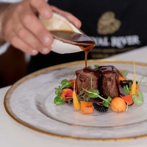 ein Mann gießt Soße auf einen Teller mit Essen