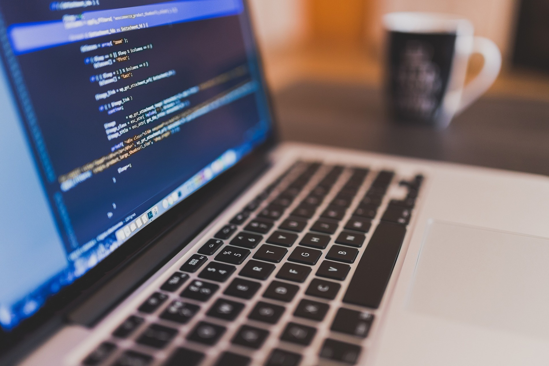 a close up of a laptop with a cup in the background