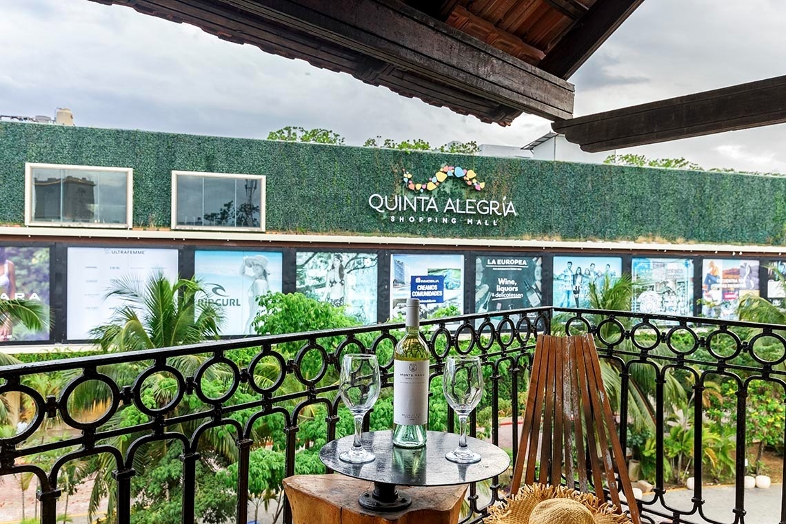 un balcón con una botella de vino y dos copas frente a un quinta alegria