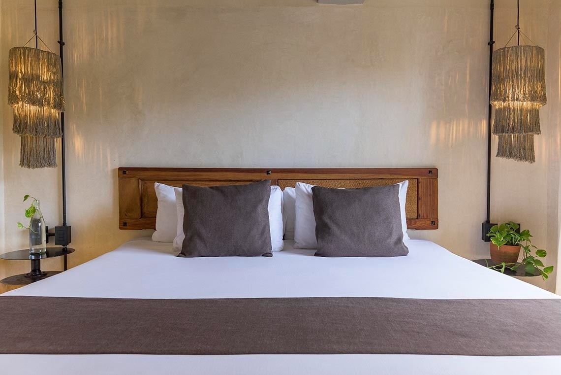 una cama con sábanas blancas y almohadas grises