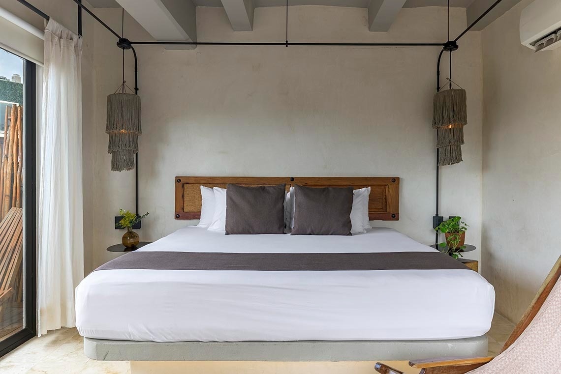 una cama con sábanas blancas y almohadas grises en una habitación