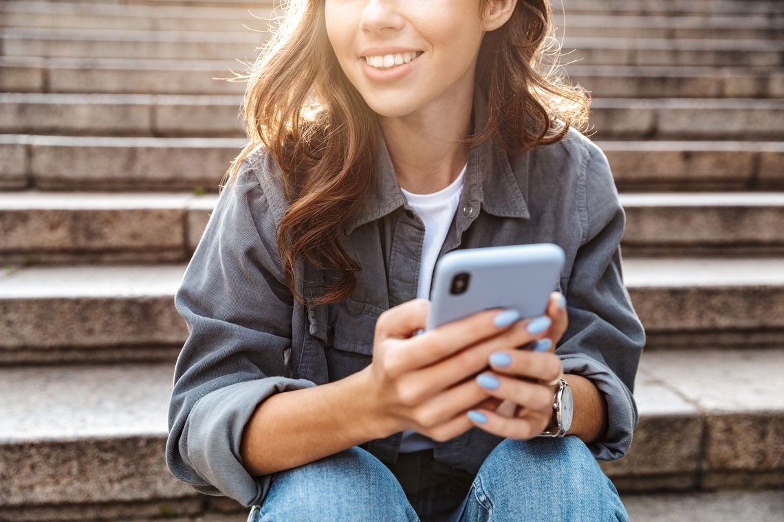 a woman with blue nails is sitting on a set of stairs looking at her phone