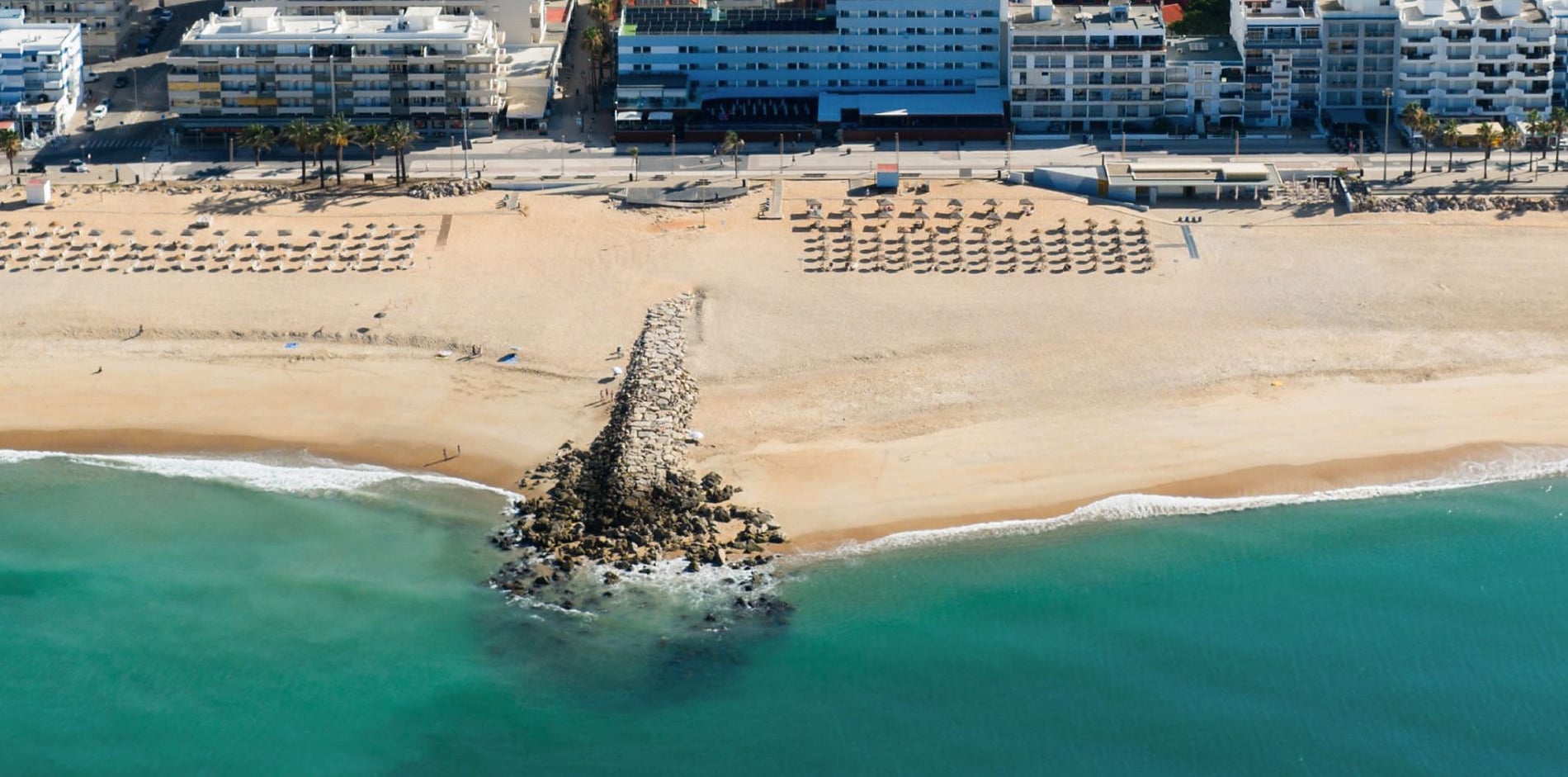 Vista aérea de hotel na praia, com cadeiras de praia e mar azul Dom Jose Beach.