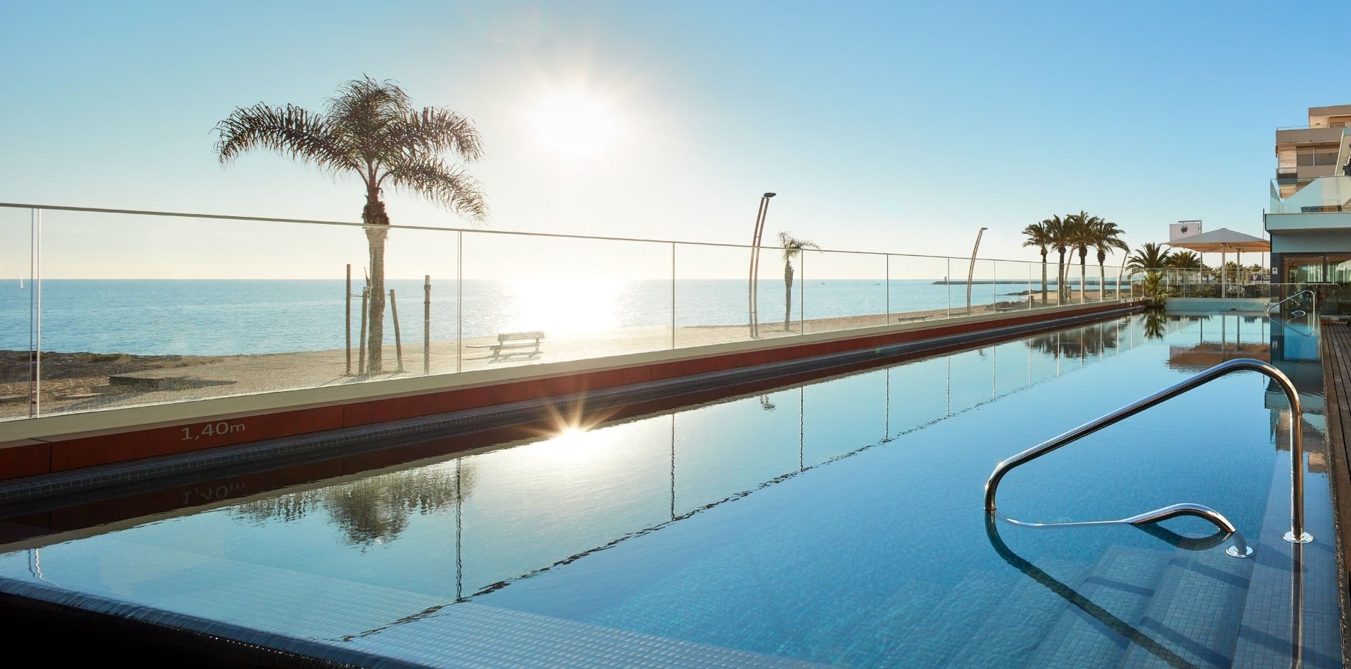 uma grande piscina com uma cerca de vidro e palmeiras ao fundo