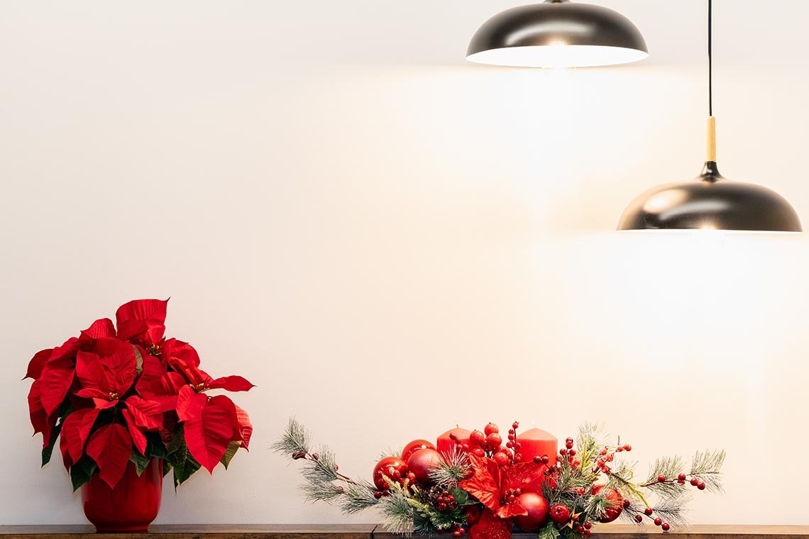 una poinsettia en un jarrón rojo junto a un arreglo navideño