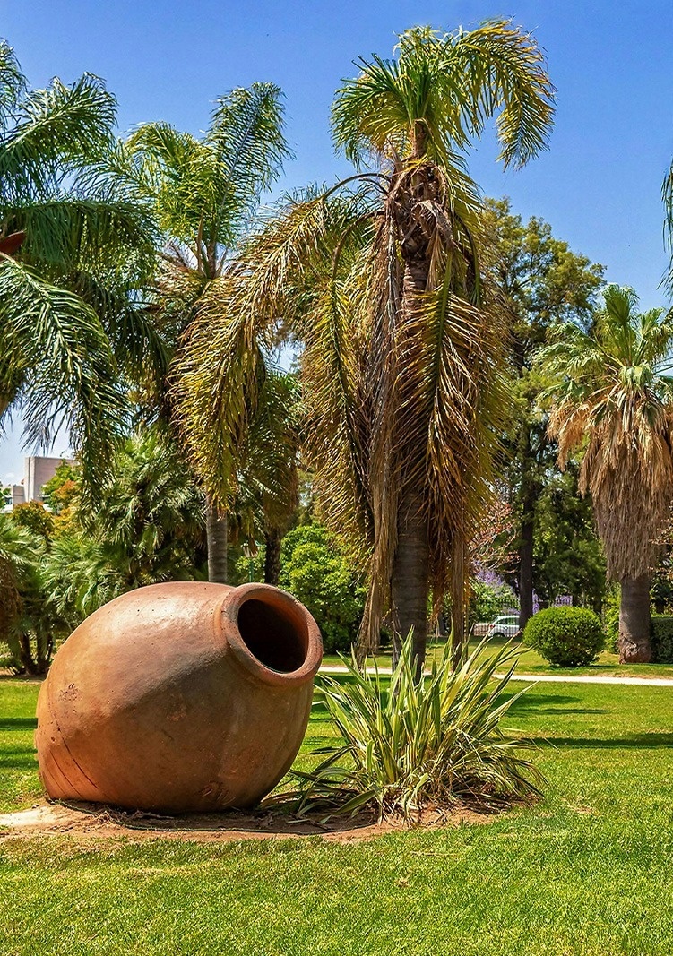 un enorme jarrón de arcilla está en medio de un parque rodeado de palmeras