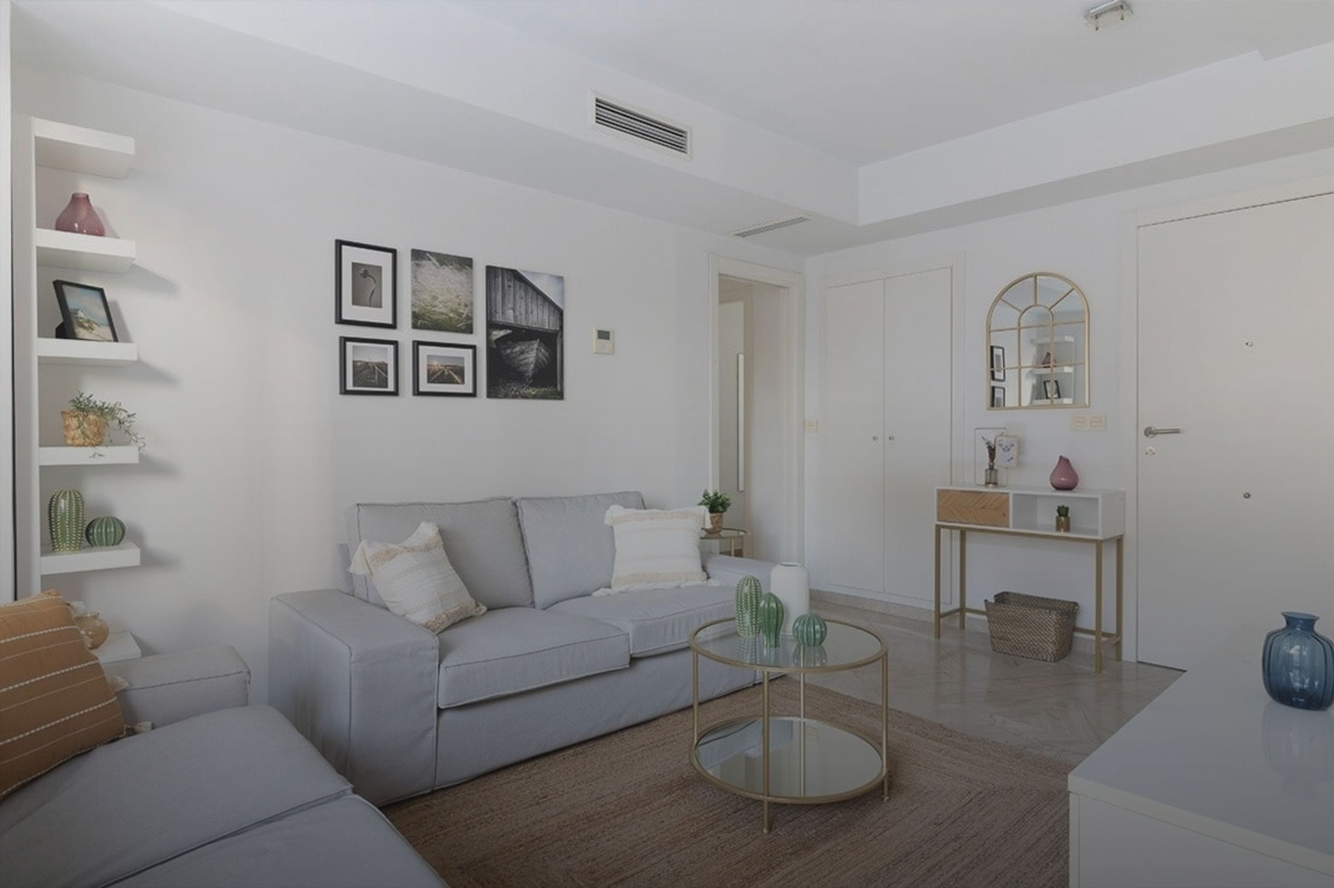 Un salón moderno y luminoso, decorado en tonos neutros, con un sofá gris, estantes flotantes y una mesa de centro de cristal.