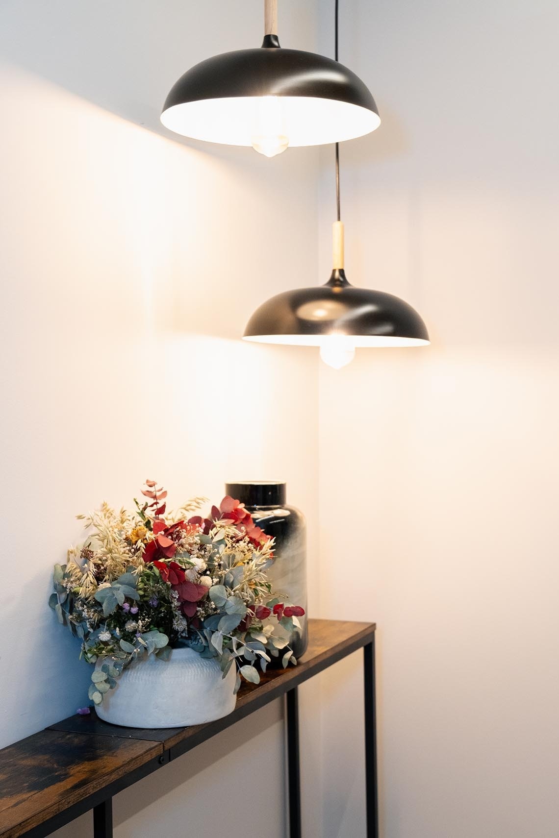 un jarrón de flores se sienta en una mesa junto a dos lámparas colgantes