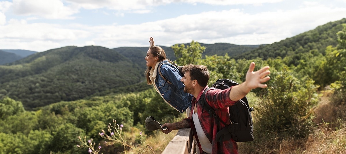 a man and a woman with backpacks are standing on top of a hill with their arms outstretched