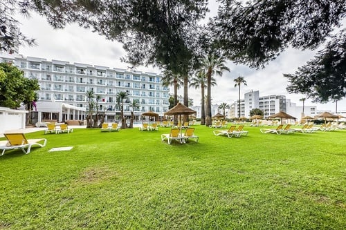 Hotel San Fermín by Dorobe in Torremolinos: sun loungers on green lawn, palm trees, white hotel building.