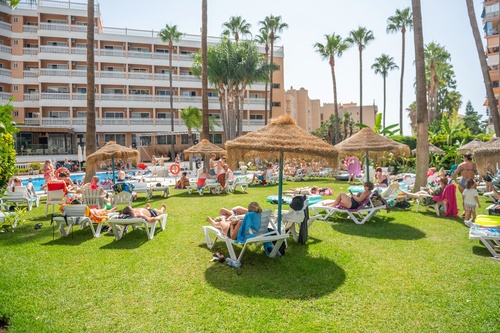 a large group of people are laying on lawn chairs under thatched umbrellas