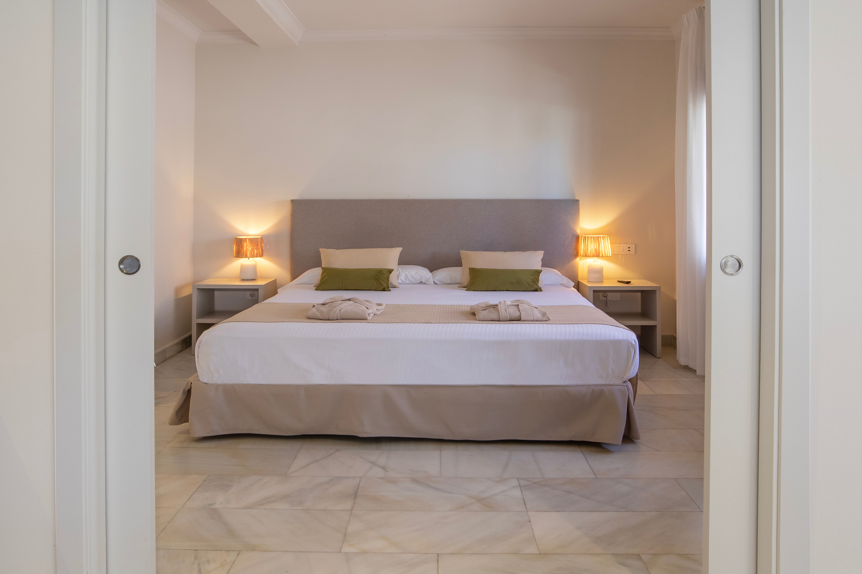 Habitación de lujo Dynastic Corporativa, cama king, mármol, mesitas de noche, lámparas.
