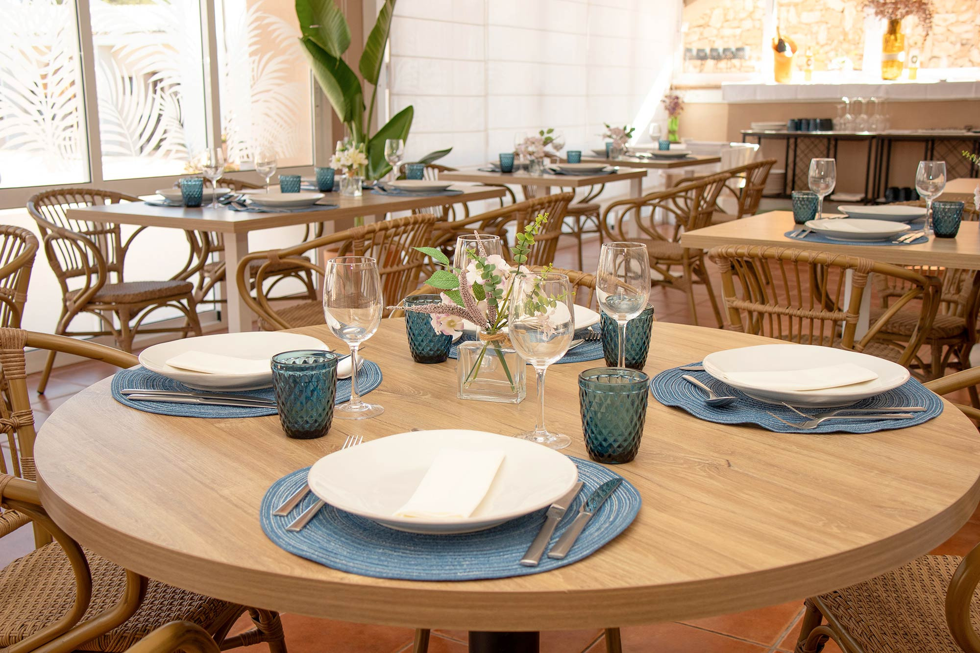 Elegante comedor de hotel, con mobiliario de madera y mimbre, y detalles azules, Dynastic Resorts.