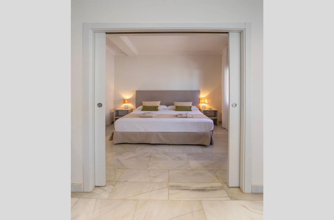 Habitación de lujo Dynastic Corporativa, cama king, mármol, mesitas de noche, lámparas.