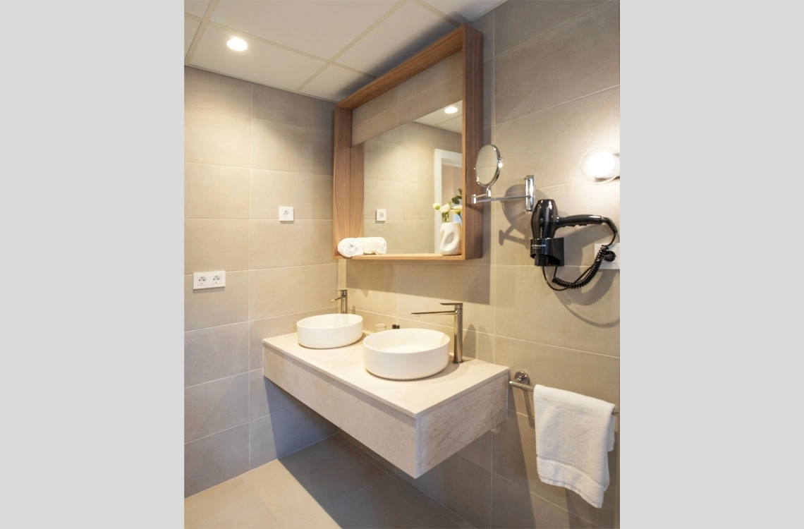 Banheiro moderno com duas pias, espelho e secador de cabelo, ideal para seu Dynastic Resorts.