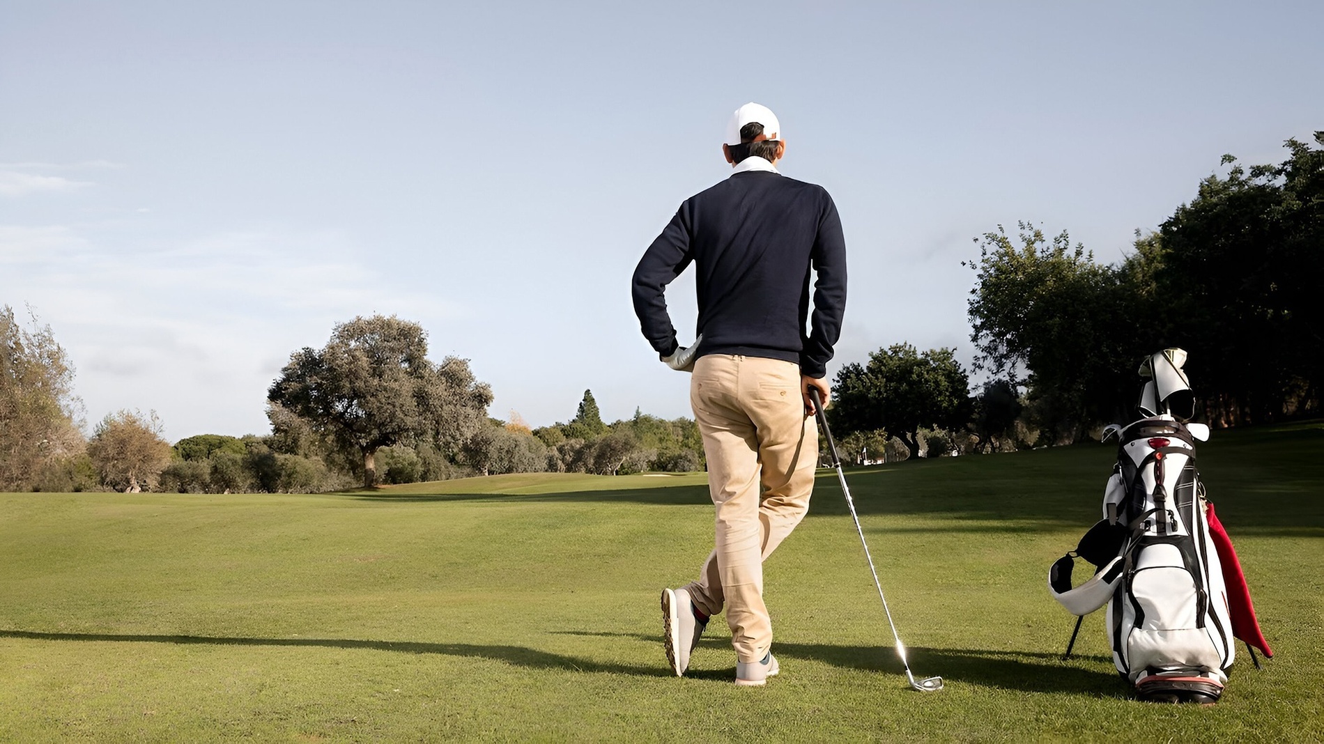 un hombre con un club de golf y una bolsa de golf camina por un campo de golf