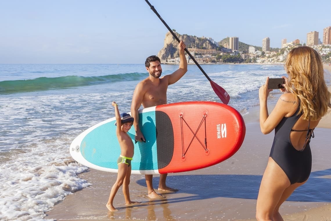 a woman taking a picture of a man holding a paddle board with the letter m on it