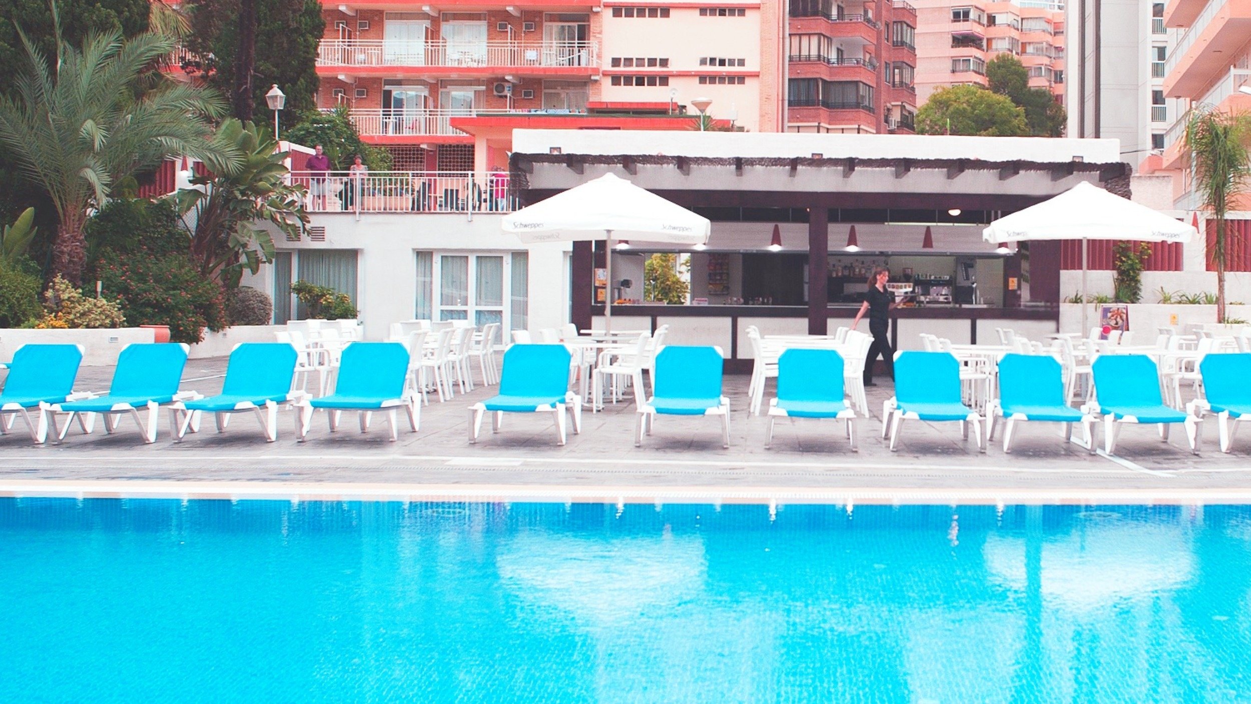 uma piscina com cadeiras azuis e guarda-chuvas brancos