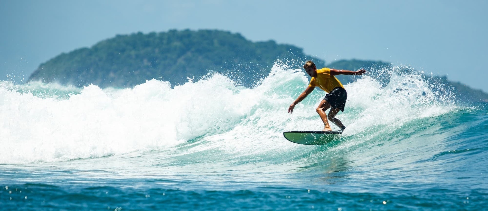 un hombre en una camisa amarilla surfea una ola en el océano
