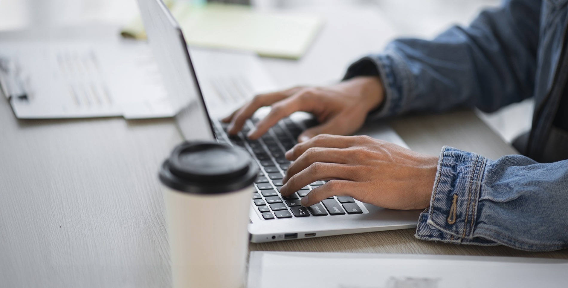 um homem está digitando em um laptop na frente de uma xícara de café