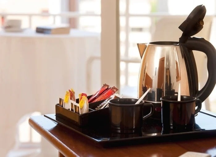 a silver kettle sits on a tray next to two cups
