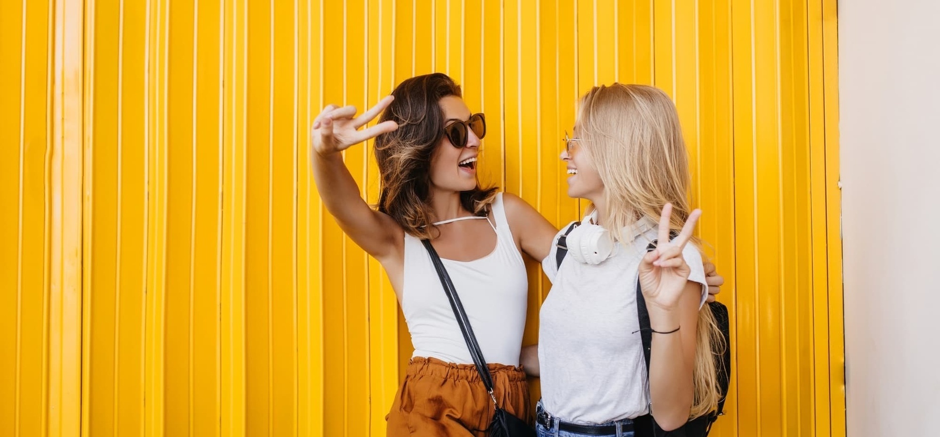 duas mulheres dão um sinal de paz ao lado de uma parede amarela