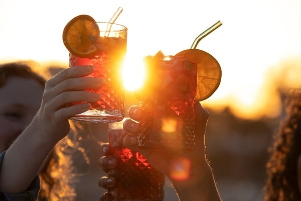 two people toasting with drinks at sunset with the sun shining through them